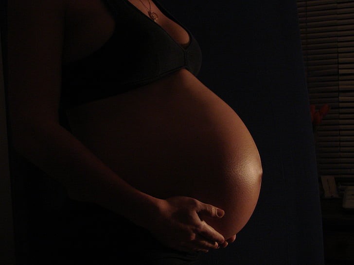 A partially unclothed black pregnant woman with bulging belly.