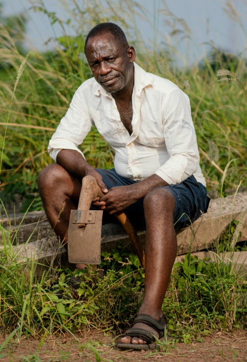 An African middle aged male farmer sitting with a hoe in hand at his farm