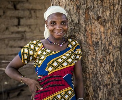 An African woman standing while leaning on a tree.
