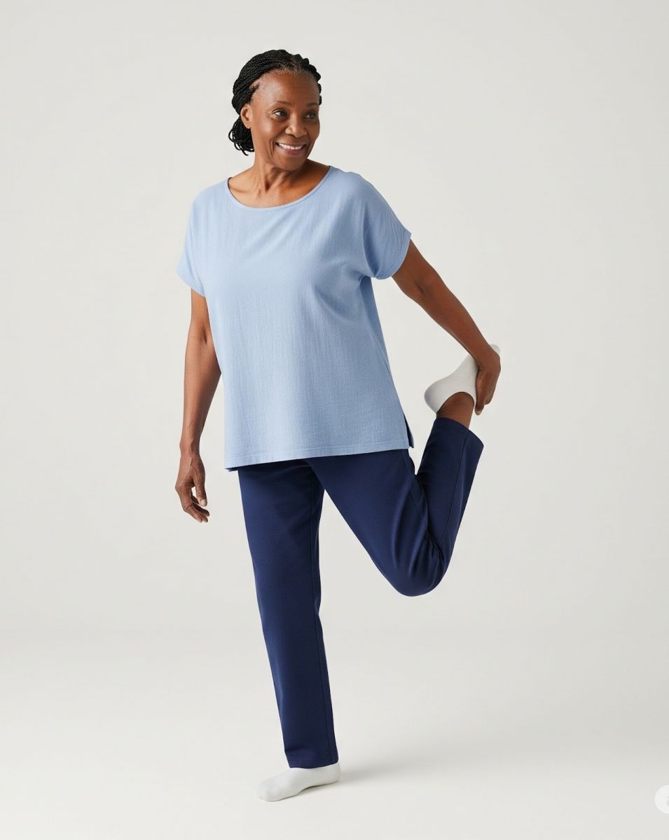 African woman in blue shirt and dark pants standing and doing a quadriceps stretch
