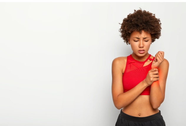 Displeased Afro-girl holding the painful wrist of her left flexed forearm