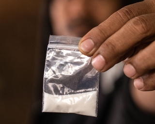Hand holding a small ziplock bag containing a white powder, cocaine