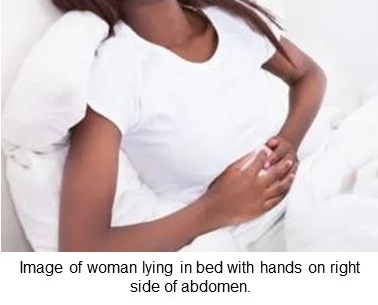 African woman lying in bed with hands on right side of abdomen.