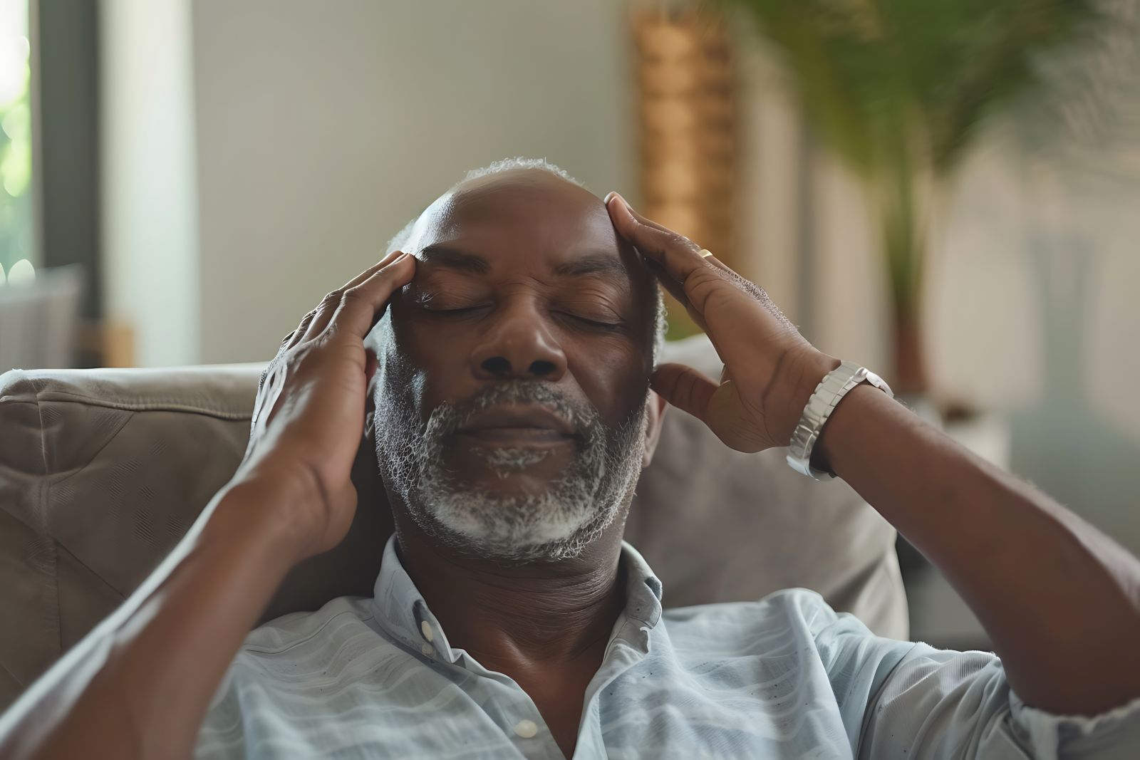 Elderly black man with both hands on his head probably due to a headache