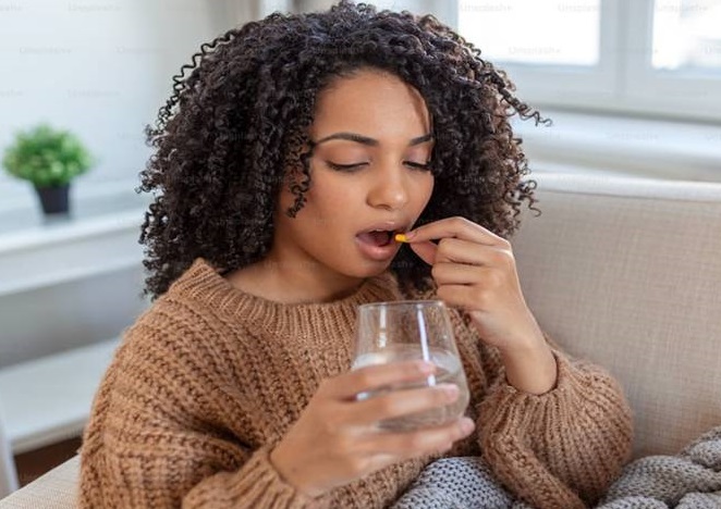 A black lady taking a pill orally with a glass of water in hand