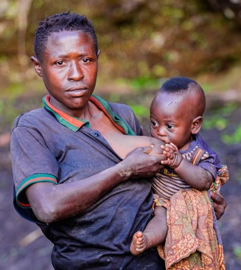An African woman breastfeeding her baby while standing outdoor.