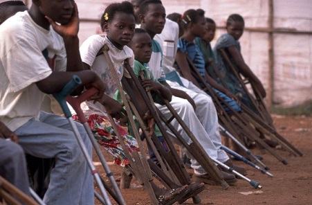 Row of African children with poliio seated outfoors holding on to their crutches