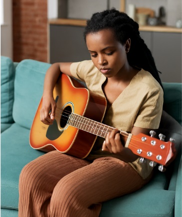 Young African girl sitting on a sofa and playing the guitra,