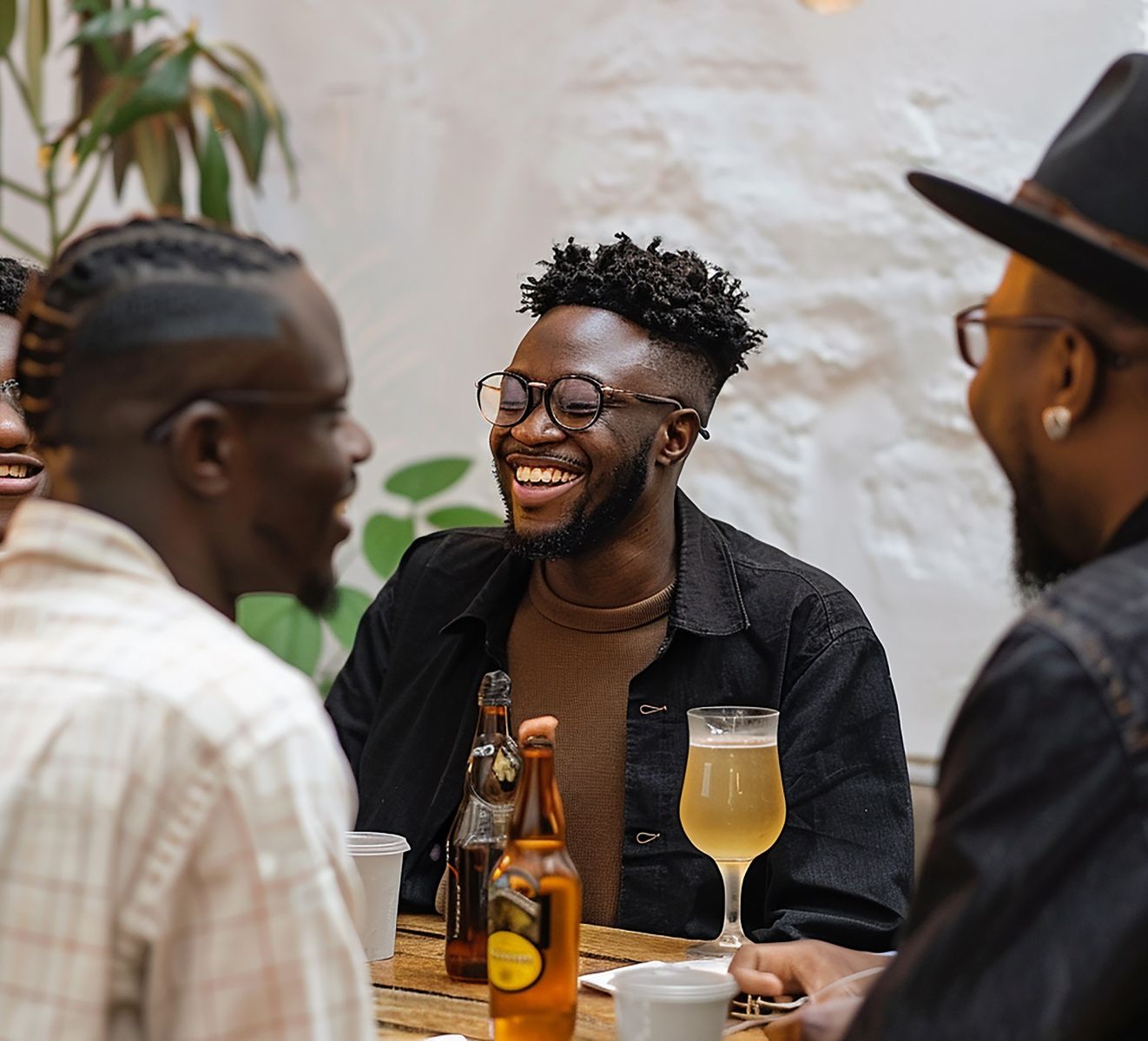 Three young Africans sitting arouns a table laughing and drinking beer