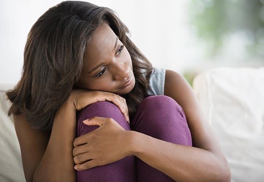 Young black woman with her head on her crouched knees and in pensive mood