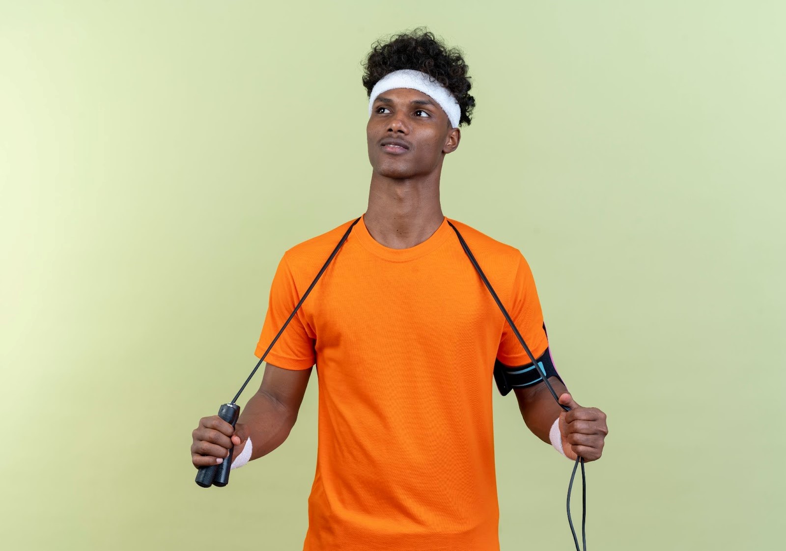 A young African male wearing bright ornage T-shirt and holding a jumping rope tightly across the back of his neck