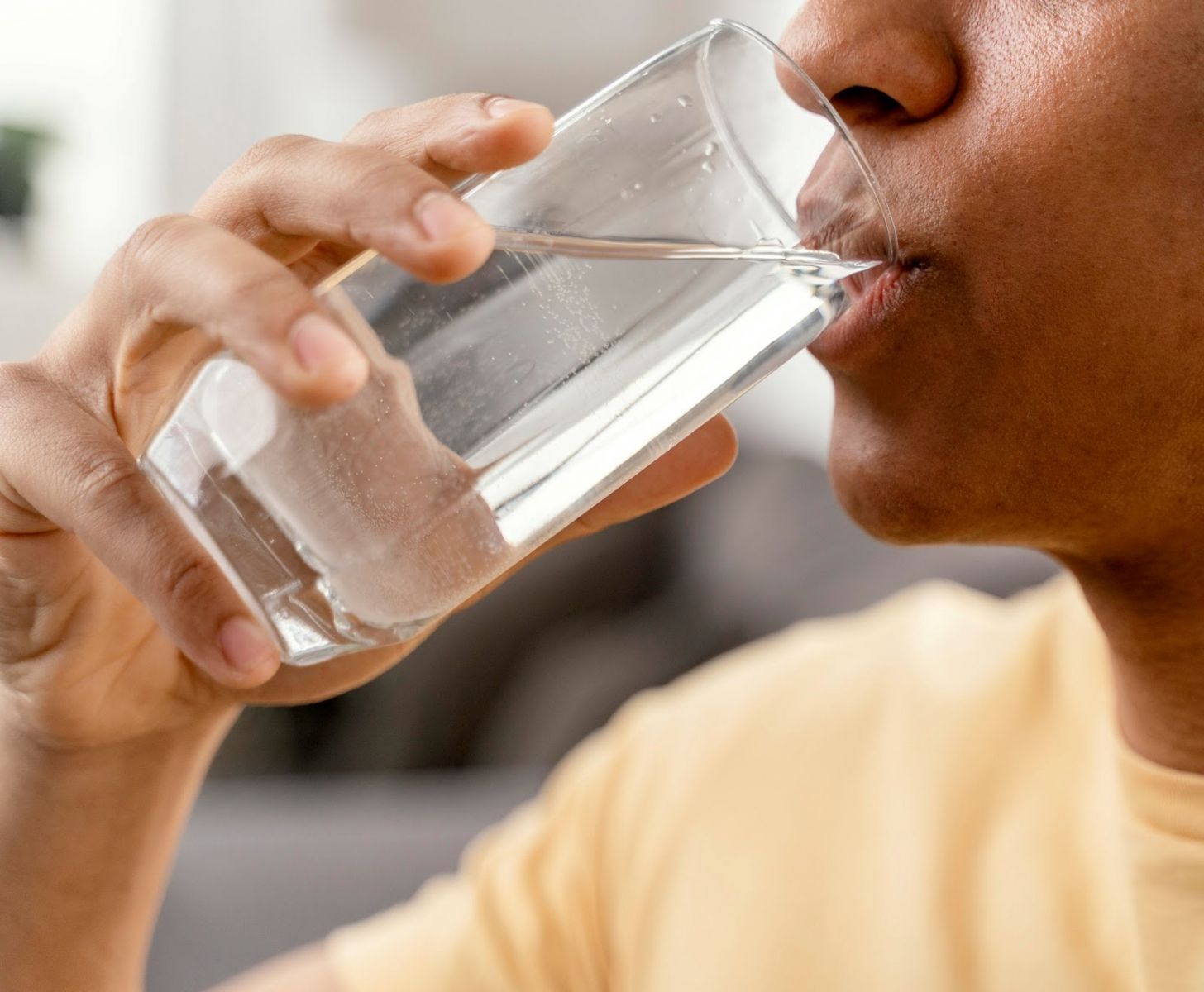 A young African male drinking water from a glass cup