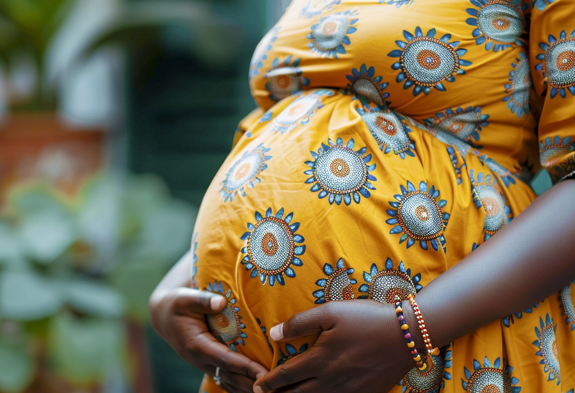 Left-sided close up of the torso of a pregnant African woman in brilliant yellow patterned gown posing outdoors