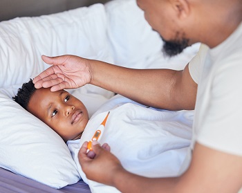 Father with  thermometer on hand checking for fever in a sick child lying on a bed