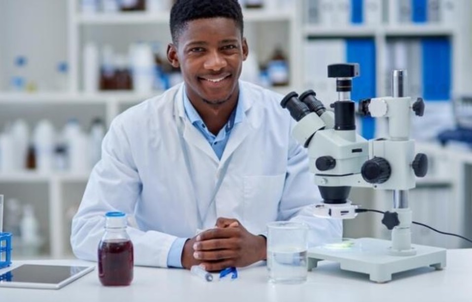 A male African MLS sitting in a laboratory at a table before a microscope