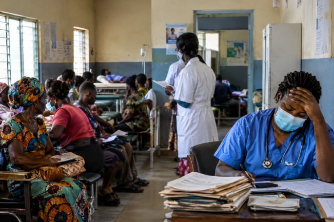 An exhausted healthcare worker sits at a desk in an overcrowded African health centre