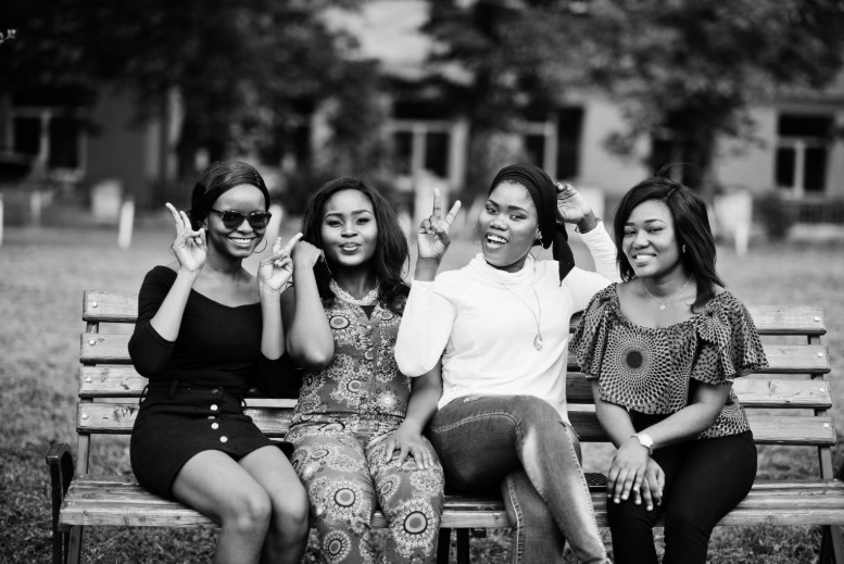 A group of young African women posing in photo while sitting together on a bench outdoor
