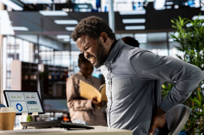 African business analyst holding on his lower back in apparent pain.