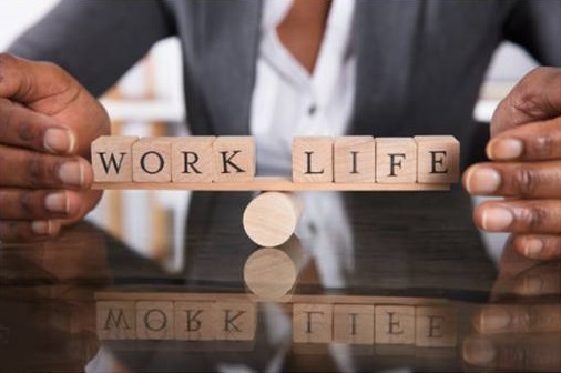 Image of an African man in professional wear holding small a set of wooden pieces that together read: Work Life Balance